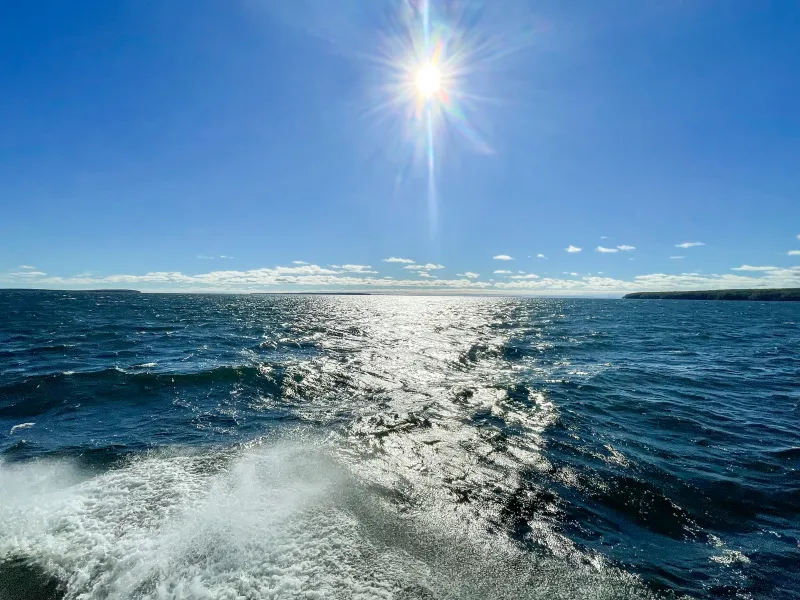 Lake Superior churning behind a boat, with the Apostle Islands in the distance and the sun directly overhead